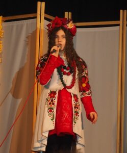 Zdjęcie przedstawia śpiewającą dziewczynkę na scenie.