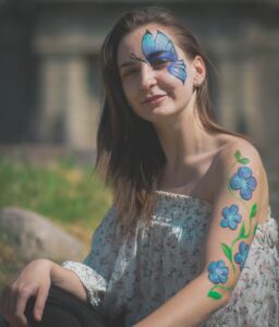 kobieta z namalowanym motylem i kwiatami uśmiecha się w stronę obiektywu aparatu